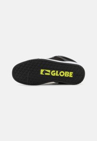 Soletta di scarpe da skate nera con grip testurizzato, accenti bianchi e un prominente logo giallo 'GLOBE'. Realizzata in materiale gommoso resistente.