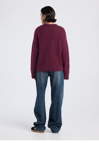 Plum knit sweater with a relaxed fit, crew neckline, and long sleeves, paired with loose blue denim jeans. Plain texture with no patterns.