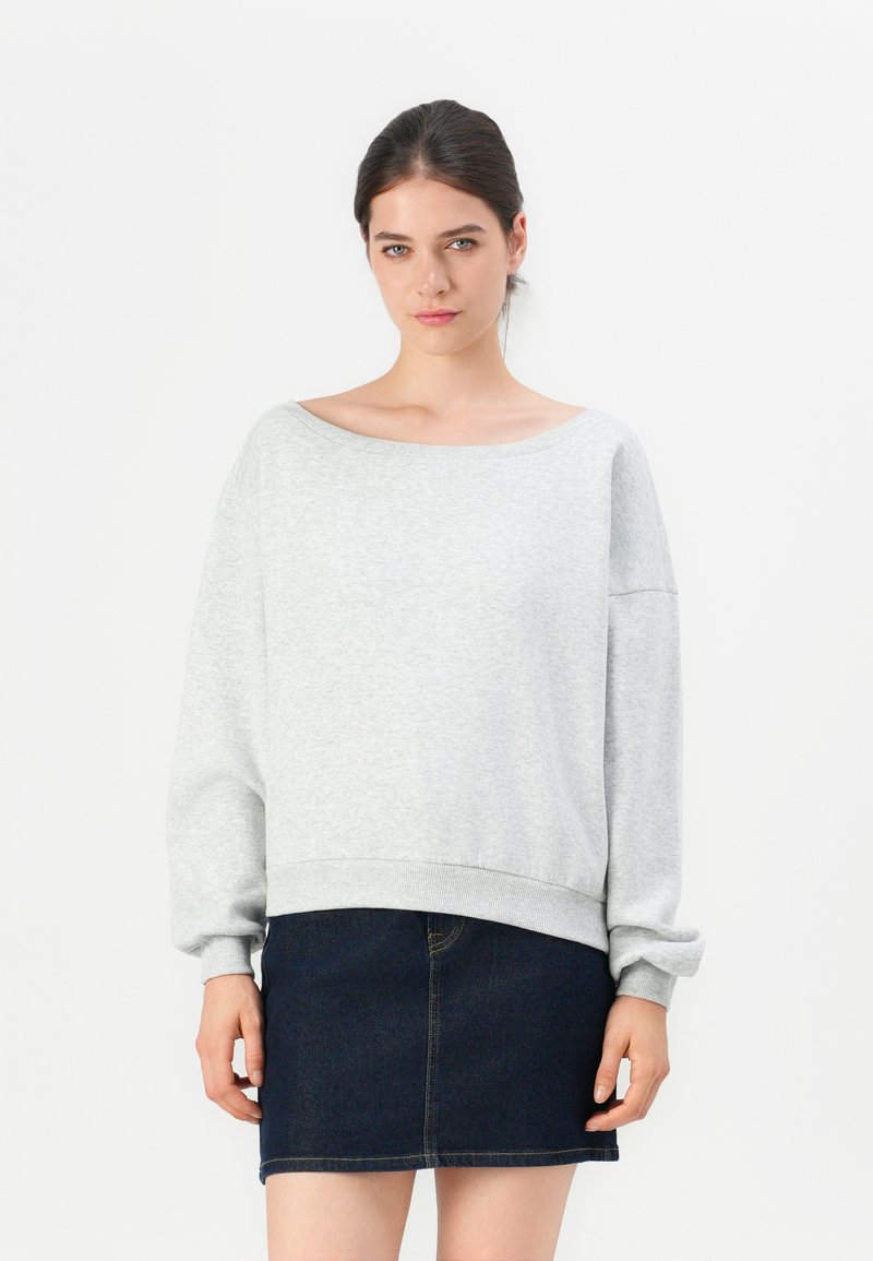 Felpa oversized grigia chiara con scollatura ampia e orlo a coste, abbinata a una mini gonna in denim scuro. Tessuto morbido con una vestibilità comoda.