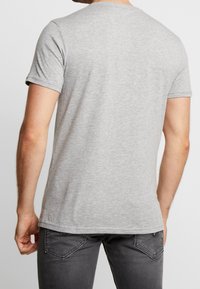Camiseta de algodón gris con mangas cortas, cuello redondo y un diseño liso; textura suave visible, combinada con pantalones vaqueros gris oscuro.