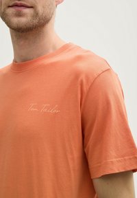 Krāsa: oranžs. Materiāls: kokvilna. T-krekls ar īsām piedurknēm, apaļo kakla izgriezumu un diskrētu izšūtu "Tom Tailor" logo uz krūšu daļas. Gluda tekstūra.