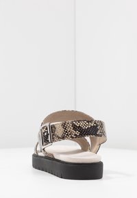 Avoin varvas sandaali musta-beige käärmeennahkakuosisella hihnalla, säädettävällä hopeisella soljella ja mustalla tekstuuripohjalla. Pehmeä beige pohja.