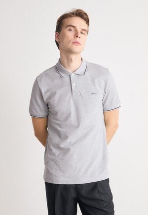 Graues Poloshirt mit klassischem Design, ausgestattet mit einer Knopfleiste mit zwei Knöpfen, geripptem Kragen und marineblauen Besätzen an den Ärmeln. Dezentes Logo auf der Brust.