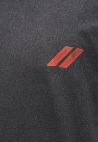 Σκούρο γκρι ύφασμα με δύο κοντές, κεκλιμένες κόκκινες ρίγες τυπωμένες κοντά η μία στην άλλη κοντά στο κέντρο δεξιά.