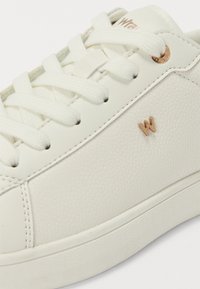 Hvit teksturert sneakers med runde lisser, et subtilt preget mønster og en liten gull "W"-logo. Har gummisåle og tømmede detaljer.