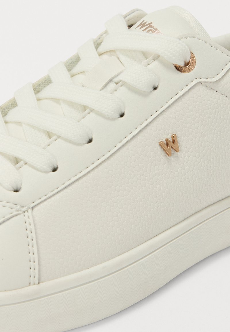 Zapatilla blanca texturizada con cordones redondos, un sutil patrón en relieve y un pequeño logo dorado con la "W". Presenta una suela de goma y acentos cosidos.