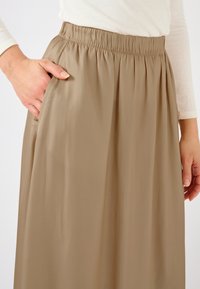 Beige rok gemaakt van lichtgewicht stof, voorzien van een elastische tailleband en zijzakken, met een gladde, vloeiende textuur.