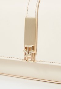 Kermainen nahkalaukku, jossa on sileä pinta, kultakuvioitu varuste ja hallitseva logoakcentti. Suljettu tyylikkäällä suorakulmaiseen lukolla.