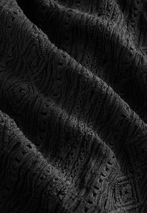 Tessuto nero strutturato con un motivo in rilievo, caratterizzato da linee ondulate e accenti circolari. La trama appare morbida e leggermente soffice.