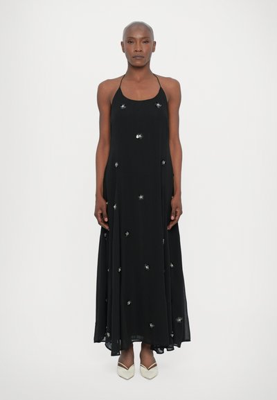 Black halter dress with a flowing silhouette, embellished with silver star-like shapes. Textured fabric drapes elegantly to the floor.
