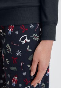 Navy pyjama set met een donkere bovenkant met geribde manchetten en een onderkant met een feestelijk patroon van notenkrakers, zuurstokken en sneeuwvlokken.