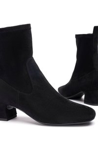 Bottines en suède noir avec un léger talon, présentant une texture lisse, un bout pointu et des découpes sur les côtés.
