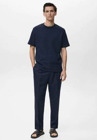 Marineblauwe geribbelde t-shirt met korte mouwen, gecombineerd met op maat gemaakte marineblauwe broek en zwarte slidesandalen. Zachte textuur, relaxte pasvorm en minimalistisch ontwerp.