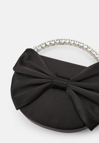 Fekete selyem clutch táska nagy masni részlettel és átlátszó strasszokkal díszített fogantyúval. Kerek forma, sima textúrával.