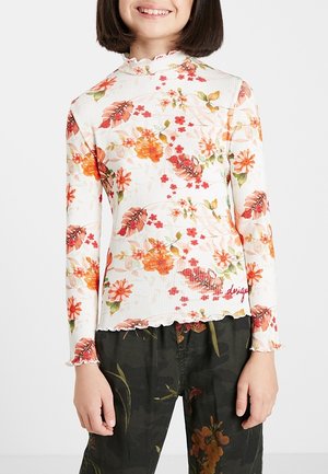 Child wearing a white long-sleeve floral top with orange and red flowers and dark floral-patterned pants.