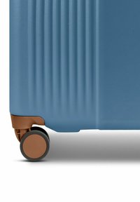 Maleta rígida azul claro con acanaladuras verticales, acento marrón en la base y una rueda negra para movilidad.