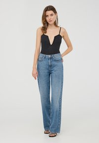 Body nero con pois bianchi e scollatura a V profonda, abbinato a jeans larghi a vita alta di un azzurro chiaro. Modello che indossa sandali con tacco neri.