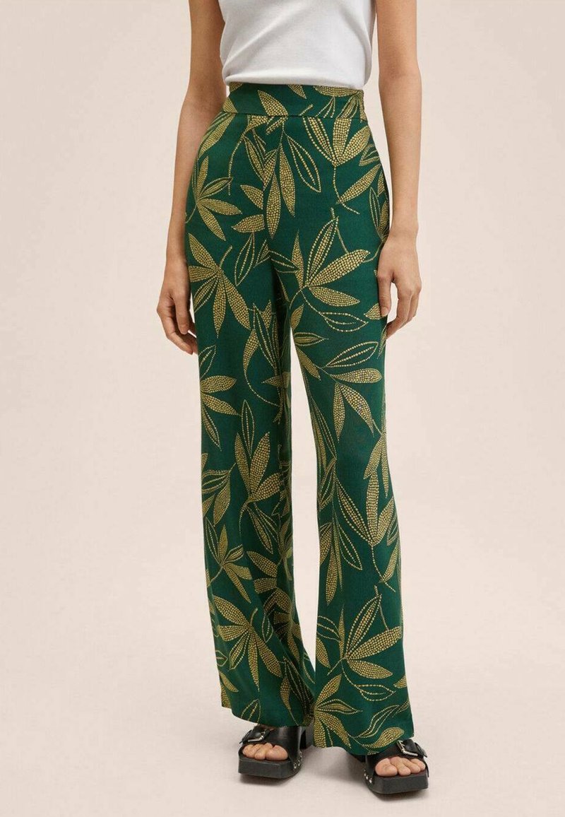 Green wide-leg pants featuring a gold leaf pattern, made of a soft fabric. The high waist complements the flowing design. Black platform shoes visible.