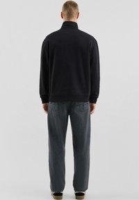 Felpa nera con collo alto e orlo a coste, abbinata a jeans in denim grigio dalla vestibilità larga con tasche posteriori e dettagli di cuciture visibili.