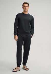 Donkergrijze lange mouwen sweatshirt en bijpassende broek van een zachte stof. Heeft een ronde halslijn en elastische manchetten. G gedragen met beige sandalen.