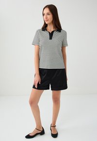 Zwart-wit gestreepte poloshirt met een zwarte kraag, gecombineerd met zwarte shorts. Bevat korte mouwen en een knoopsluiting.