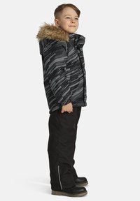 Mustra musternad musteljak, millel on karvaga vooderdatud kapuuts, kantuna mustade pükste ja mustade saapadega. Jakil on tõmblukk ja elastsed varrukad.