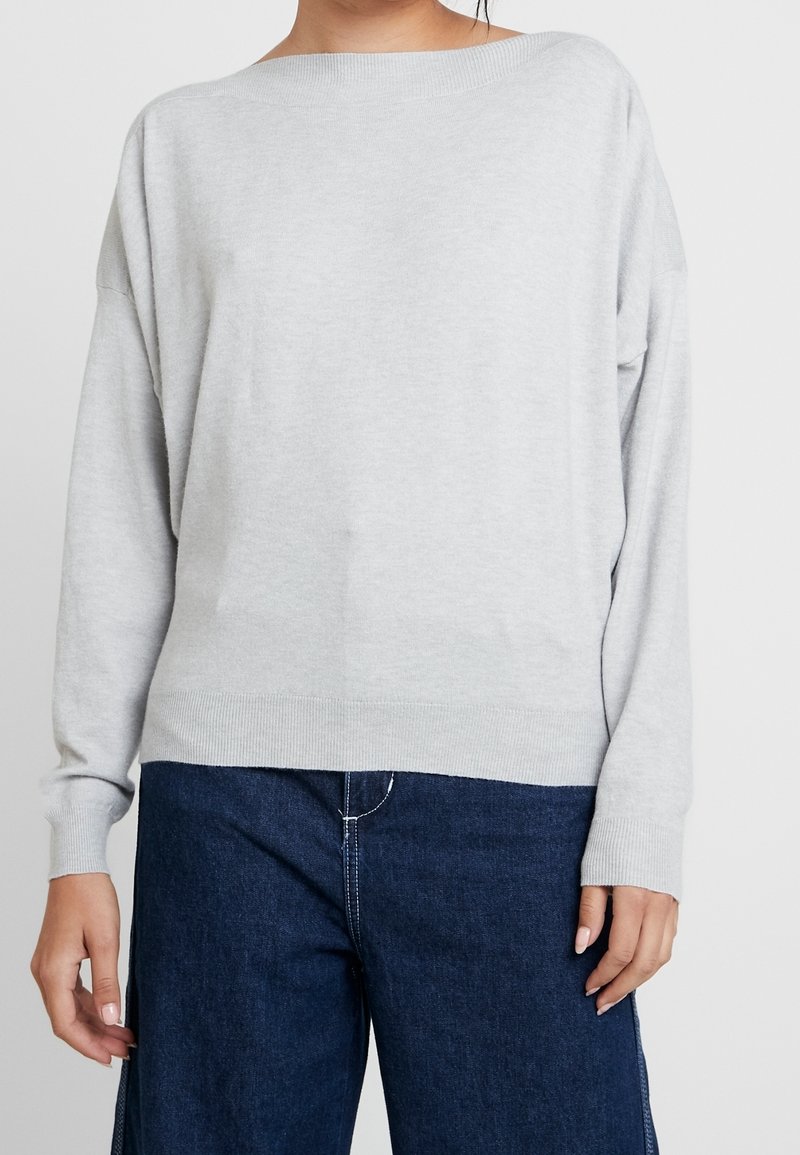 Pull oversize gris clair avec un col large et des manches longues, doté de poignets et d'un ourlet côtelés, associé à un pantalon large bleu foncé.