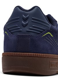 Granatowy sneaker z zamszową cholewką, gumową podeszwą, teksturowanym obcasem i neonowymi akcentami. Posiada wyściełany kołnierz oraz logo marki.