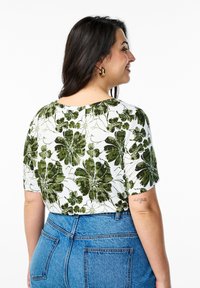 Trumpas rankovėmis baltas marškiniai su žaliu gėlių raštu. Suderinta su aukštu liemeniu mėlynomis džinsinėmis kelnėmis, suteikiančiomis laisvą siluetą.