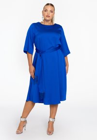 Satin blauwe jurk met een strik taille, 3/4 mouwen en franjes. Kenmerkt zich door een vloeiend A-lijn ontwerp, een gladde textuur en een knielange zoom.