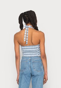 Top halter azul e branco em padrão xadrez, com costas franzidas, combinado com jeans de cintura alta em azul claro. Apresenta um fecho com laço no pescoço. Textura suave.