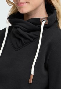 Felpa nera con colletto alto e arricciato, dotata di lacci bianchi. Presenta un tessuto a maglia testurizzata e dettagli in pelle marrone vicino al collo.