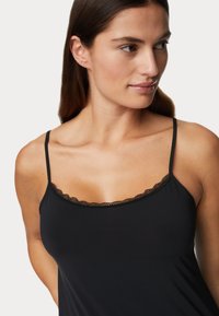 Camiseta negra de tirantes finos, con un delicado encaje en el escote. Material suave y elástico, con un ajuste a medida.