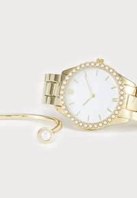 Montre en or avec une lunette accentuée de perles, un cadran blanc et un bracelet en or. Comprend un bracelet manchette assorti en or avec un détail en perle.