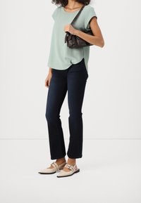 Haut vert clair à manches courtes, jean évasé bleu foncé, ballerines beiges pointues avec détails de bride, et sac à main foncé. Design simple et décontracté.