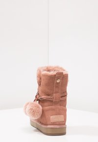 Růžové kotníkové boty s umělou kožešinou, vyrobené z texturované tkaniny, s kulatým pom-pom akcentem a plochou gumovou podrážkou. Obsahují dekorativní šněrování.