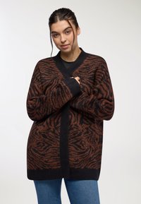 Brązowy i czarny kardigan w wzory, z dekoltem w kształcie V, długimi rękawami i luźnym krojem, wykonany z miękkiego, teksturowanego materiału.