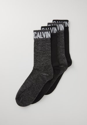 Tres pares de calcetines: un par negro liso, dos con un patrón texturizado gris oscuro, que presentan la marca blanca "CALVIN" en los bordes superiores.