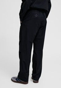 Zwarte cargobroek met een elastische tailleband, met zijcargozakken, een gladde textuur en een klein logo op de achterkant van de tailleband.