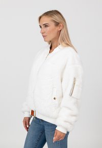 Weiße Kunstpelz-Bomberjacke mit gerippten Bündchen, Reißverschlusstaschen und goldfarbenen Hardware-Details. Weicher Stoff und lässige Passform.