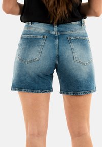 Shorts in denim con un lavaggio blu chiaro, design aderente, con due tasche posteriori, texture scolorita e orlo sfilacciato.