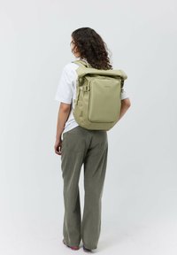 Zaino impermeabile verde con chiusura a roll-top, spallacci regolabili, tasca frontale con zip e una finitura liscia opaca.