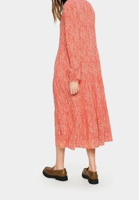 Červené a bílé šaty s potiskem, dlouhými rukávy, se sukňovým designem ve více vrstvách a volným střihem. Nosit s hnědými mokasíny a černým topem pod nimi.