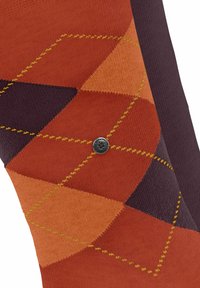 Chaussette avec un motif argyle orange, marron et violet et une petite plaque en métal ronde portant l'inscription "Turlington The Original."