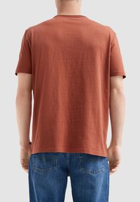 Roestkleurig T-shirt met korte mouwen van zacht, textuurstof met een ronde hals en een ontspannen pasvorm, gecombineerd met blauwe spijkerbroeken.