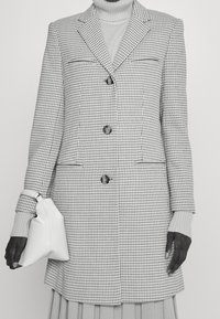 Rutig kavaj i svart och vitt tyg, med snedskurna slag, två knappar och framfickor; matchad med en vit handväska.