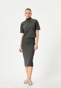 Haut en tricot gris à côtes avec un col montant, associé à une jupe crayon de longueur genou assortie. Des ballerines en ton argent complètent le look.