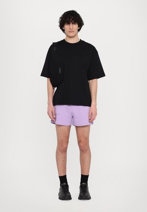 Svart oversized t-skjorte, lyse lilla shorts, svarte sko og en svart crossbody-veske. Glatt stoff, avslappet passform, minimalistisk design.