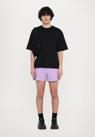 Černé oversized tričko, světle fialové šortky, černé boty a černá křížová taška. Hladká tkanina, volný střih, minimální design.