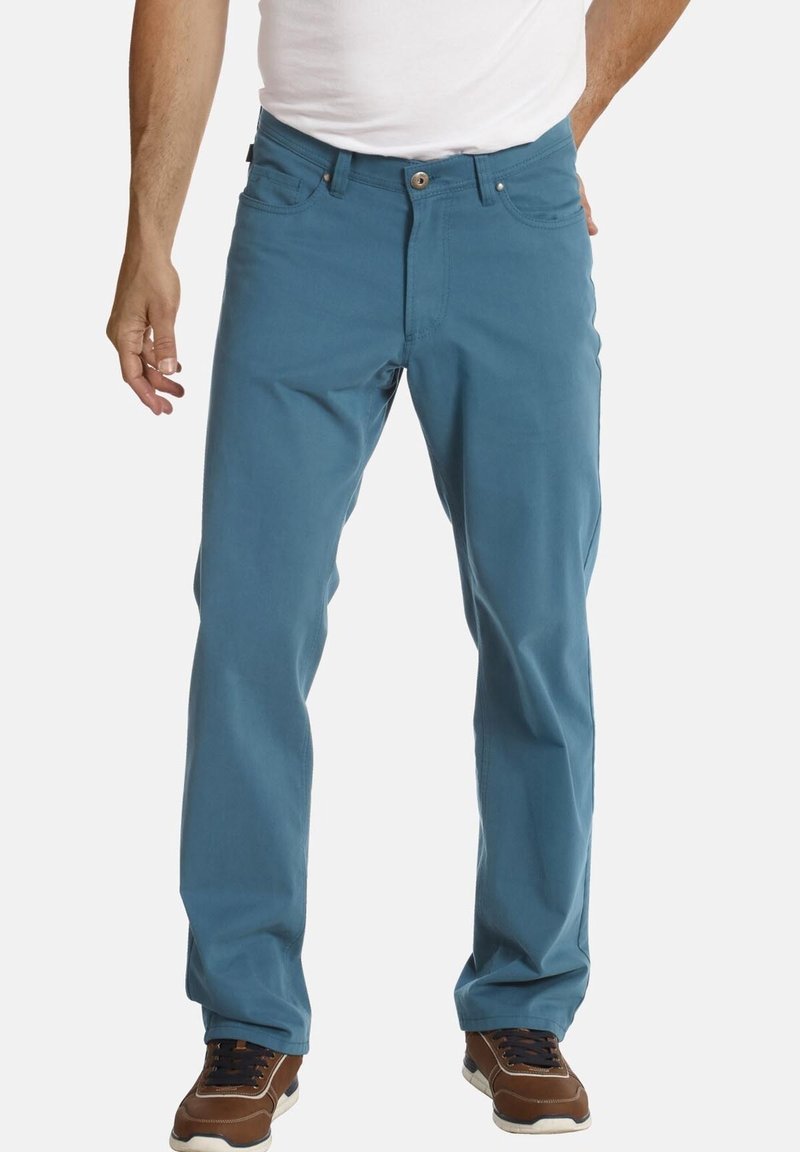 Blaue Baumwollhose mit geradem Bein, ausgestattet mit fünf Taschen und einem Knopfverschluss. Kombiniert mit braunen und weißen Sneakers.